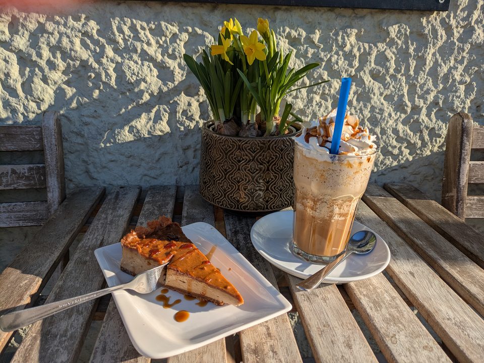 Kuchenstück mit Karamell und Eiskaffee auf einem Holztisch in der Sonne