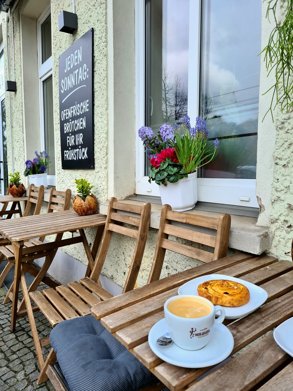 Cappuccino und Gebäck auf einem Holztisch vor dem Café